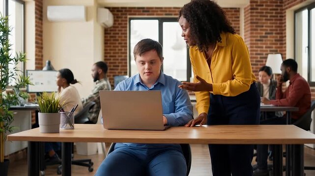 Manager explaining something to employee with Down syndrome in his new job on a laptop in a diverse office with blurred people working in the background