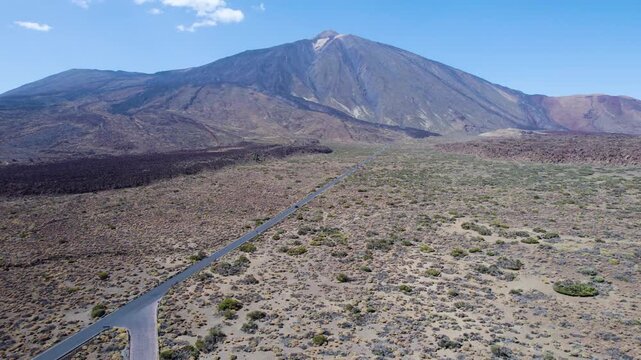 Aerial drone footage moving forward toward Teide Volcano along a straight road, with a distant car visible crossing the volcanic landscape in Tenerife, Spain.