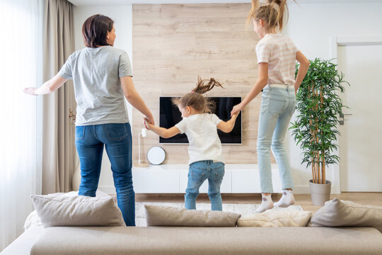 Mother and two daughters having fun jumping on a sofa in living room