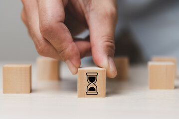 Time management concept. Self-discipline, organization, and prioritizing tasks. Project timeline and due date. Wooden cube block with hourglass icon on grey background and copy space.
