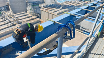 Safety lifeline hook attached to a steel railing at a high construction site, with a worker wearing...