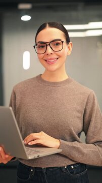Professional woman smiling with laptop in hands, exuding confidence and happiness. Dedicated person, focused on work, enjoying modern office environment. Positive and friendly demeanor.