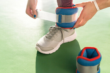 Woman putting on ankle wights before she starts a workout in a gym, health and fitness concept