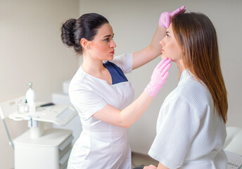 Professional cosmetician examining face skin of girl in clinic of esthetic cosmetology
