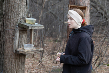 Young caucasian woman with a worried expression looking at an empty bird feeder in an autumn forest, seeking birds feeding stations.
