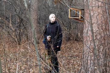 Young caucasian woman holding bird seed, looking perplexed at empty bird feeder in autumn forest, concept of wildlife interaction