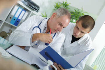 Fototapeta premium senior and junior male doctors looking at file