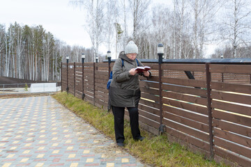 elderly woman reads a guidebook while leaning against a wooden fence, enjoying the quiet outdoors. Concept of cognitive health and relaxation.