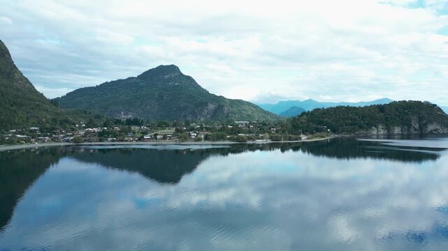 Forward drone aerial of Llifen town on Ranco Lake with mirror reflections, mountains backdrop, and serene Chilean wilderness panorama