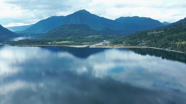 Panning drone aerial of Ranco Lake with mirror reflections, mountains backdrop, cloudy sky, and serene Chilean wilderness landscape