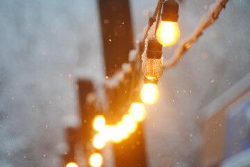 A frozen, burnt-out light bulb. Street lighting. Snowfall.