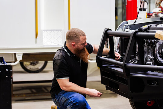 Male Aussie mechanic kneeling on the floor working on front bumper of white vehicle