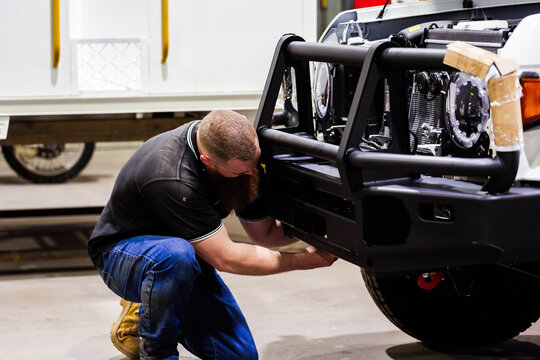 Male Aussie mechanic kneeling on the floor working on front bumper of white vehicle