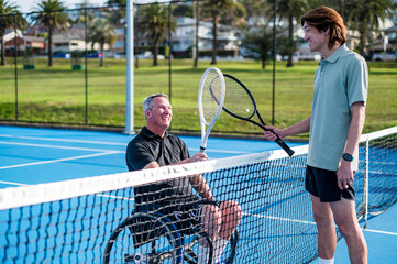 Two tennis players, one in a wheelchair, share a moment on a blue outdoor court during daytime