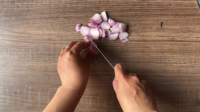 Top view of hands slicing fresh shallots on wooden cutting board