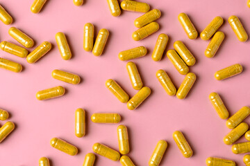 Yellow turmeric supplement capsules spread across pink background, bright flat lay with copy space for health promotion.