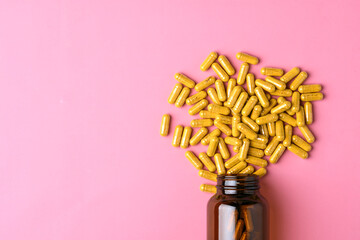 Amber supplement bottle spills yellow capsules on pink pastel background, clean minimal concept with wide copy space for branding.