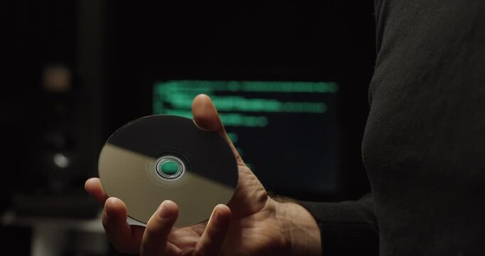 Cinematic close-up of a person holding a blank CD with a blurred code-filled monitor behind&mdash;concept for AI data storage, media archiving, legacy formats, and digital security.