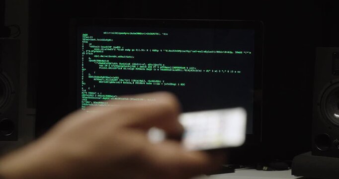 Shallow-focus shot of a hand using a remote control aimed at a monitor showing code&mdash;concept for AI control, automation, smart systems, remote management, and future technology interfaces.