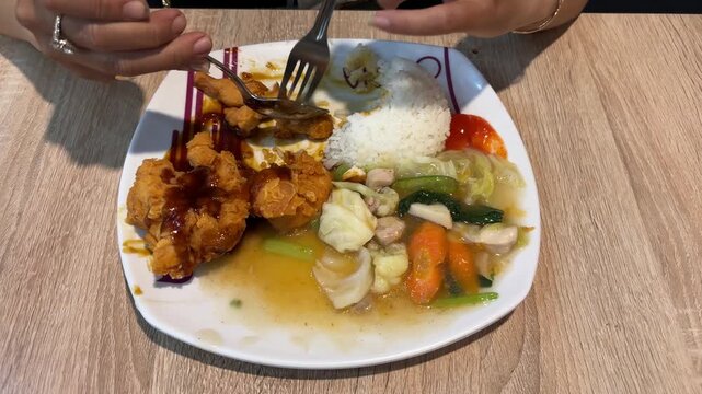 Close up of a woman's hand eating crispy fried chicken with white rice and stir-fried vegetables.