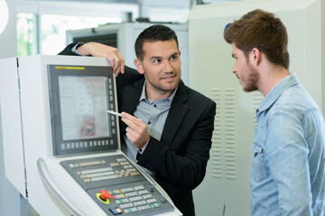suited man training apprentice technician to use computer monitor