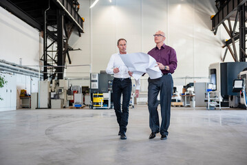 Business meeting in production hall with employees discussing blueprints