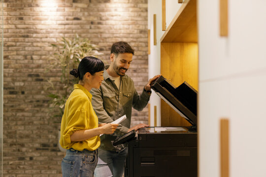 Coworkers collaborating on printing documents in a modern office