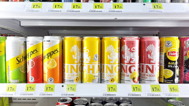 A vibrant shelf of chilled canned drinks, soda cans, including brands like Schweppes and Singha. Variety of colors, brands, and flavors beckon a refreshing experience. Thailand, December 24, 2025