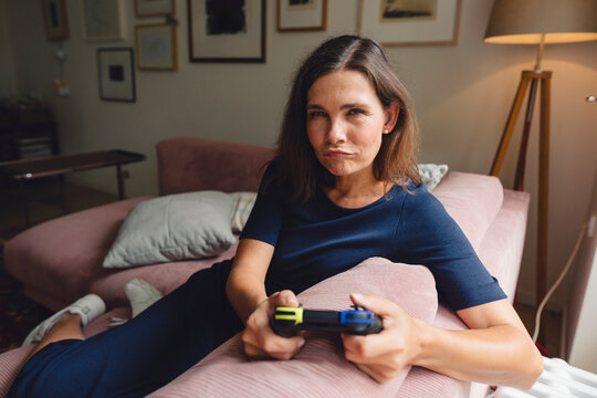 Woman holding game controller and sitting on sofa at home