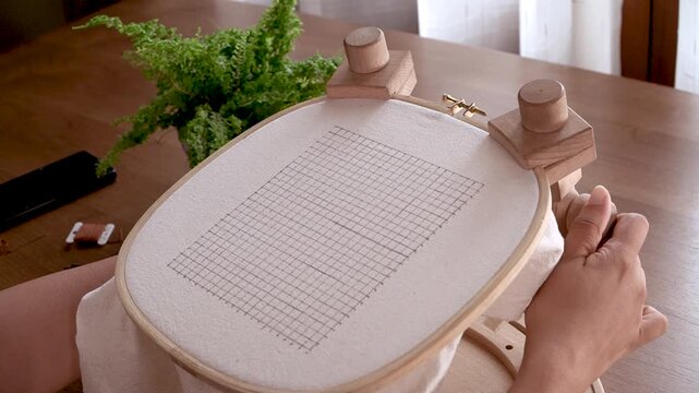 Securing the Frame: Hands Tightening the Screw on an Embroidery Hoop Stand.