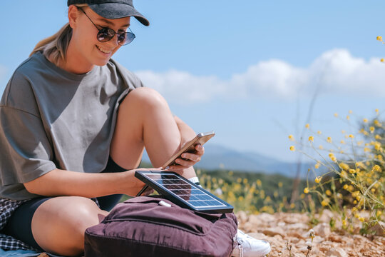 Outdoor solo traveler using solar panel to charge phone in mountain nature