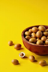 A wooden bowl overflowing with organically grown nuts, nestled amongst several more scattered on a vibrant yellow surface, one nut is shown halved to reveal its creamy interior.