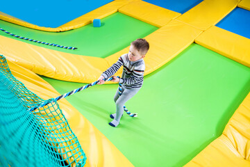Little boy playing in trampoline center jumping and climbing with rope