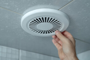 A man's hand checking a bathroom ventilation grille. Air circulation and humidity control for hygiene.