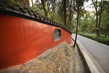Red wall with traditional tiled roof along a paved path in a tree-lined park