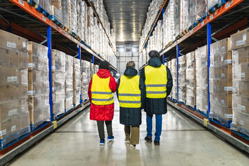 Logistics workers in safety vests walking through a low temperature cold storage warehouse with pallet racks and inventory