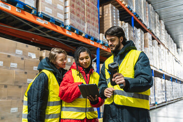 Diverse team of logistics workers collaborating and managing inventory using a digital tablet and barcode scanner in a modern cold storage warehouse