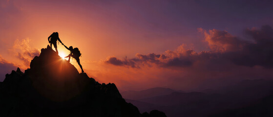 Colleagues stand together on a mountaintop at sunset, silhouetted as one person helps another reach the top with bright colors in the sky