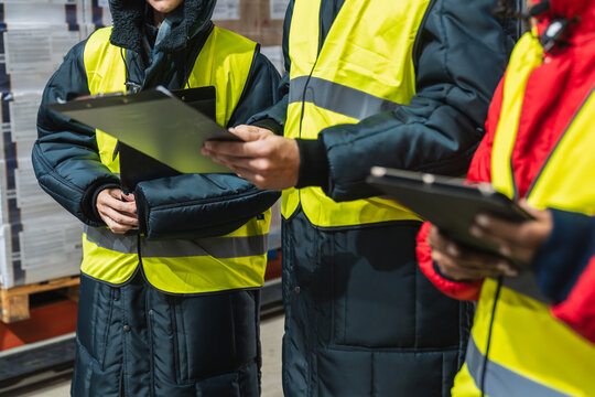 Workers in protective gear reviewing documents and managing inventory in a low temperature cold storage warehouse facility