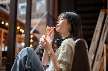 Asian woman tourist drinking coconut water while sitting on wooden bench in shopping mall or market.