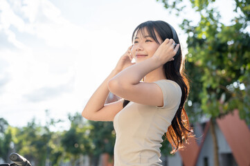 Pretty asian woman holding headphones listening to music while riding bicycle in park or city plaza. © bongkarn