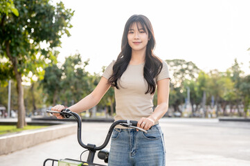 Pretty asian woman holding green rental bicycle walking on pavement in park or plaza under sunlight.