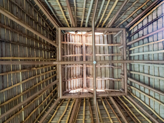 Symmetrical upward shot of a rustic palapa ceiling showing intricate wooden beams and dried palm leaves in a tropical structure in Huatulco, Oaxaca, Mexico.