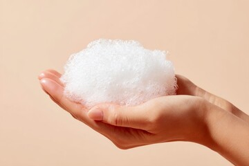 Female hands holding thick white cleansing foam or soap bubbles on a beige background demonstrate skin care routine and cosmetic products