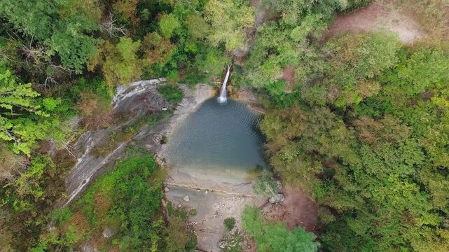 Aerial view looking directly down at a forest waterfall with a nearby path and open field in Civorio, Italy.