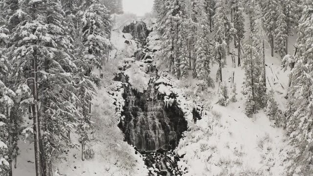 Slow-motion pull-out shot from the base of Twin Falls, revealing the massive granite headwall and the crystalline, ice-covered expanse of the Mammoth Lakes basin.