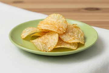 Crispy potato chips served on a green plate with wooden background  