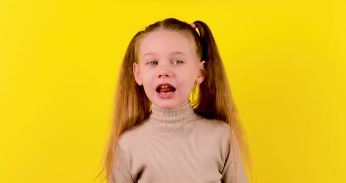 4K footage of a Caucasian girl sticking out her tongue against a yellow background, expressing playfulness, teasing, or a funny emotional reaction.