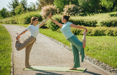 A pair of women perform a synchronized yoga pose on a path surrounded by greenery, embodying harmony and balance.