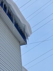 The facade  building on a cloudy day, a block of snow hanging from the eaves.